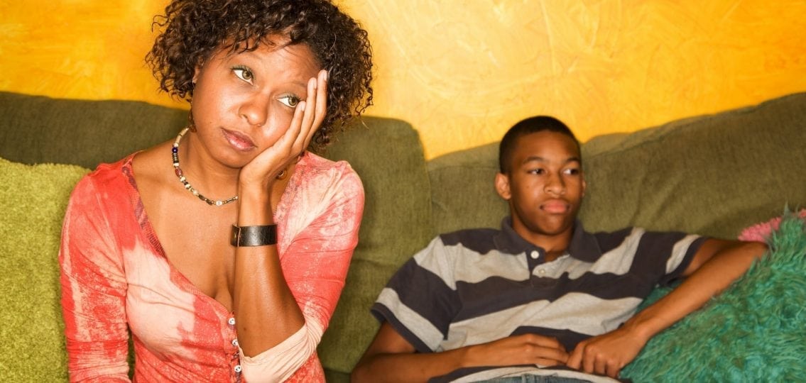 parenting problems annoyed mom with head in hands next to slumped teen boy on couch