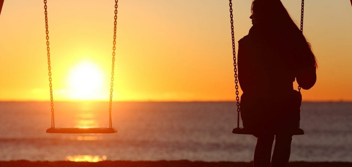 Lonely teenage daughter swinging on a swing at sunset