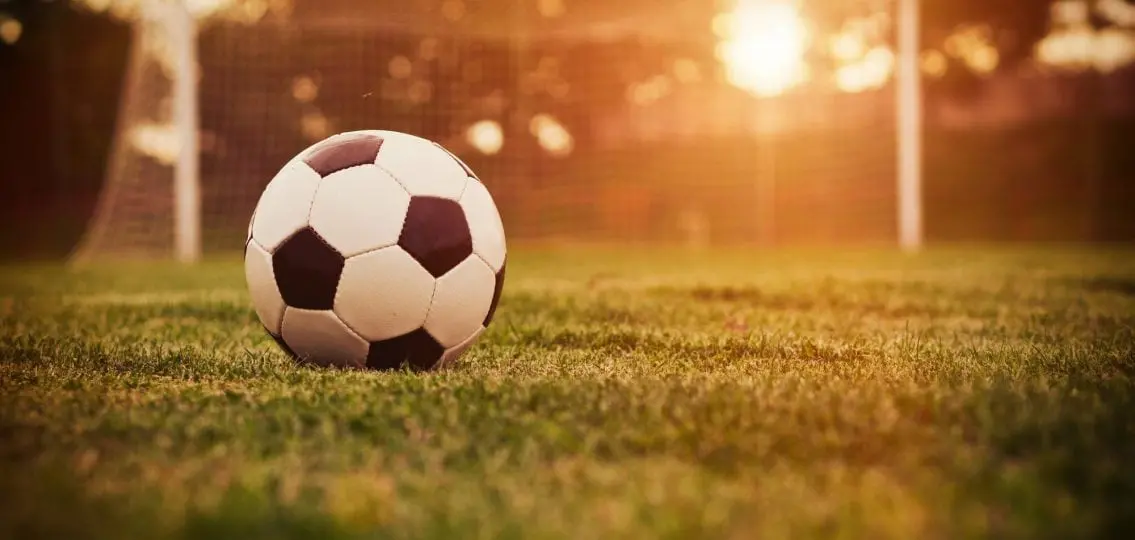 soccer ball on field in front of goal at sunset