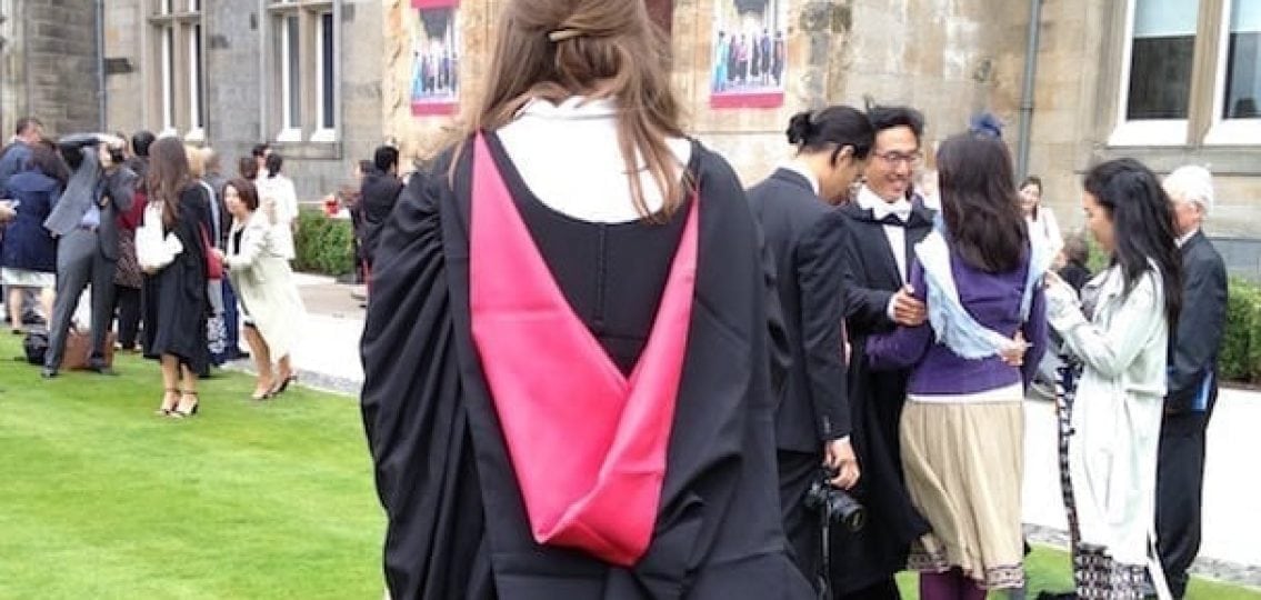 a picture of a high school graduate in graduate robes from behind outdoors