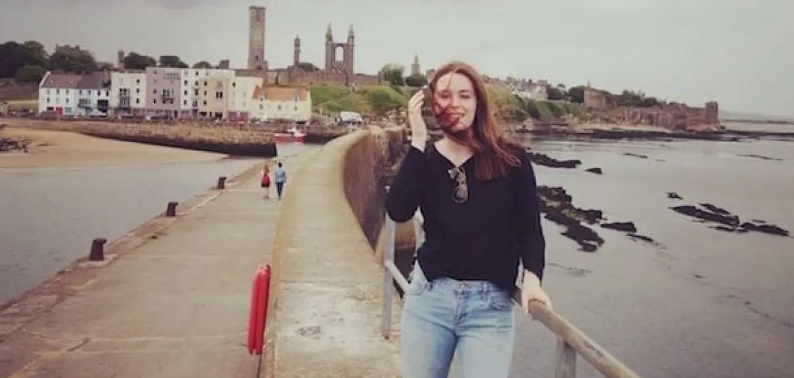 college student standing on a pier in front of St. Andrews University in the UK