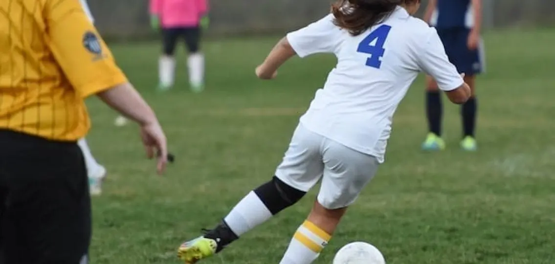 teen girl soccer player about to kick ball, other players in background referee in foreground
