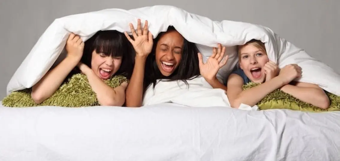 teen girls at a slumber party screaming excitedly under a duvet