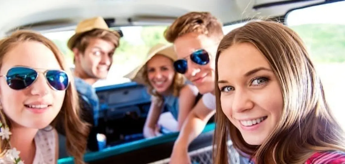 group of teenagers dressed for summer taking a selfie in a car