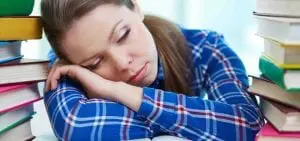 exhausted tired teenage girl falling asleep at her desk with her head in her hands surrounded by textbooks