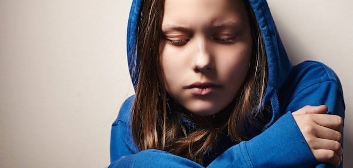 upset teen girl in hoodie hugging herself