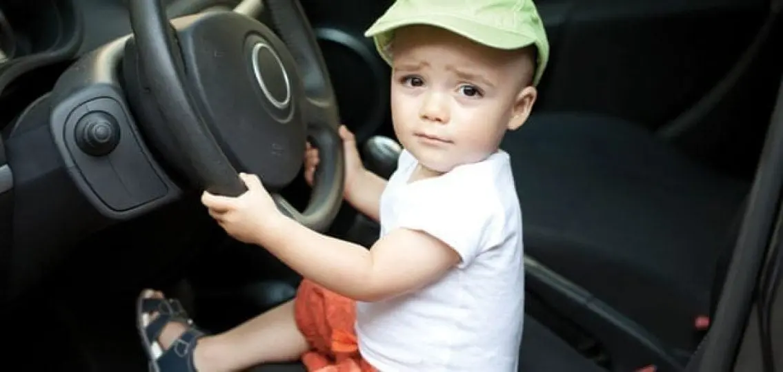 concerned baby sitting behind the wheel grabbing the steering wheel to drive