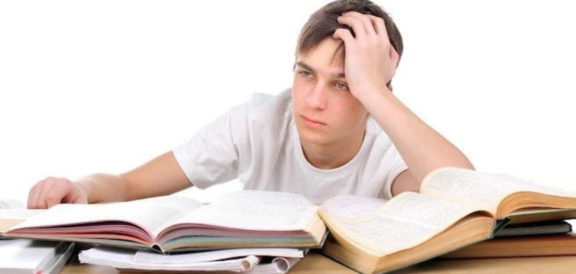 upset teenage boy in front of piles of unfinished homework
