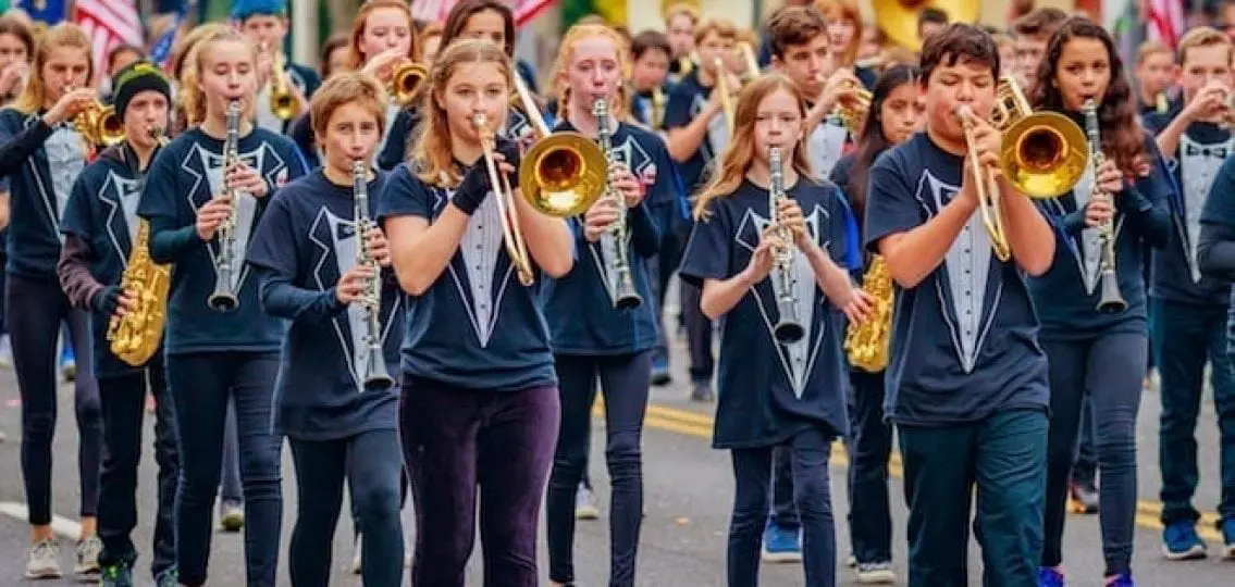 a high school band performing in a parade all wearing tuxedo t-shirts