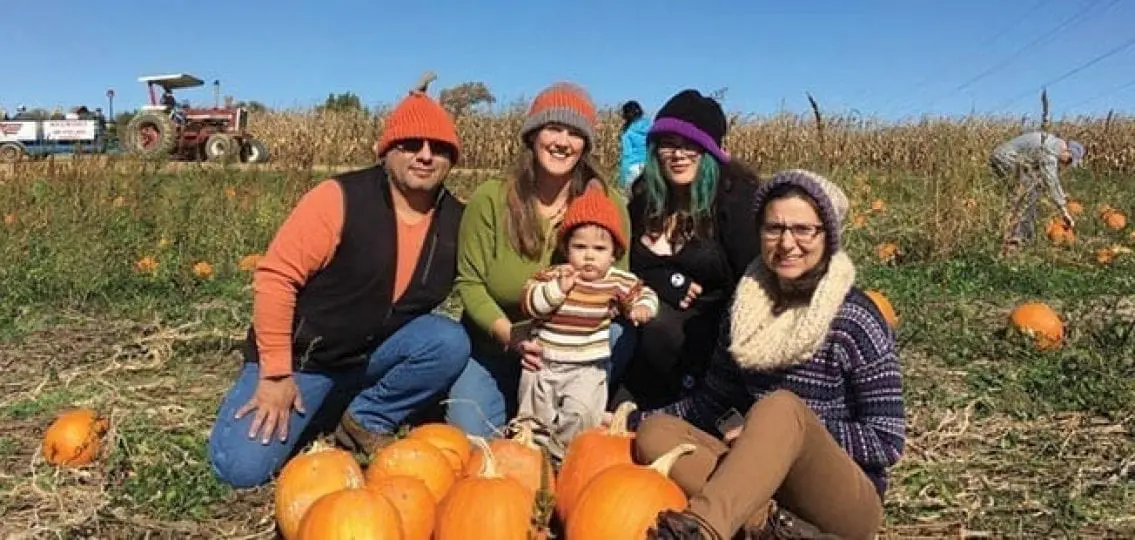 family at a pumpkin field with two older teen daughters and a one year old baby