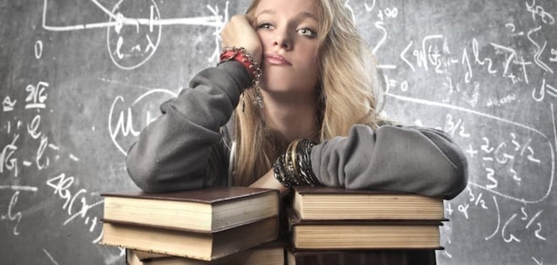bored teenage girl leaning on thick books with equations on the wall behind her