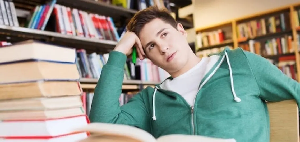 bored teenage boy with open book in library at summer school