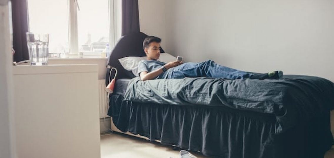 teenage boy sitting on bed alone in room on phone