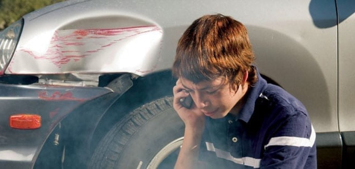 crying teenage boy on a phone call after a car accident sitting next to his dented car