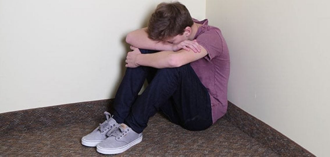 crying teen boy sitting curled up in a corner