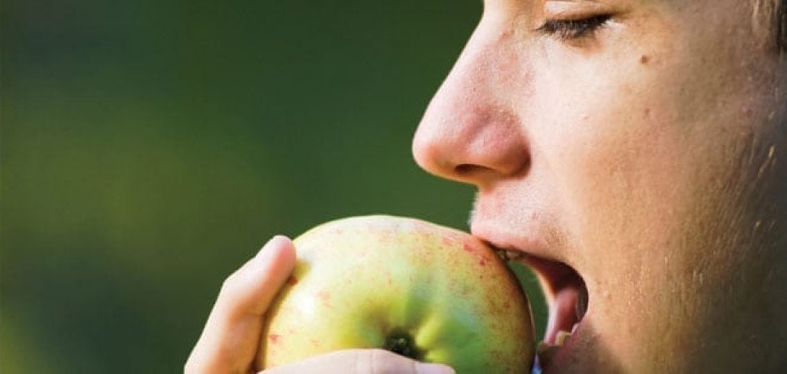closeup teenage boy eating an apple green background