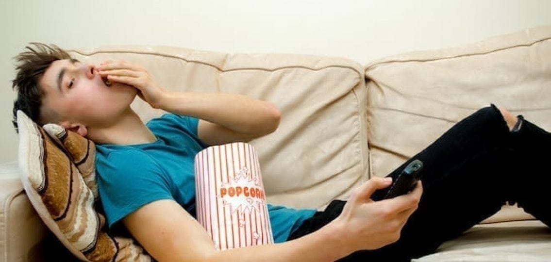 teenage boy eating popcorn while sitting on the couch
