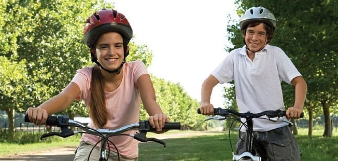 two smiling tweens on bikes in the summer