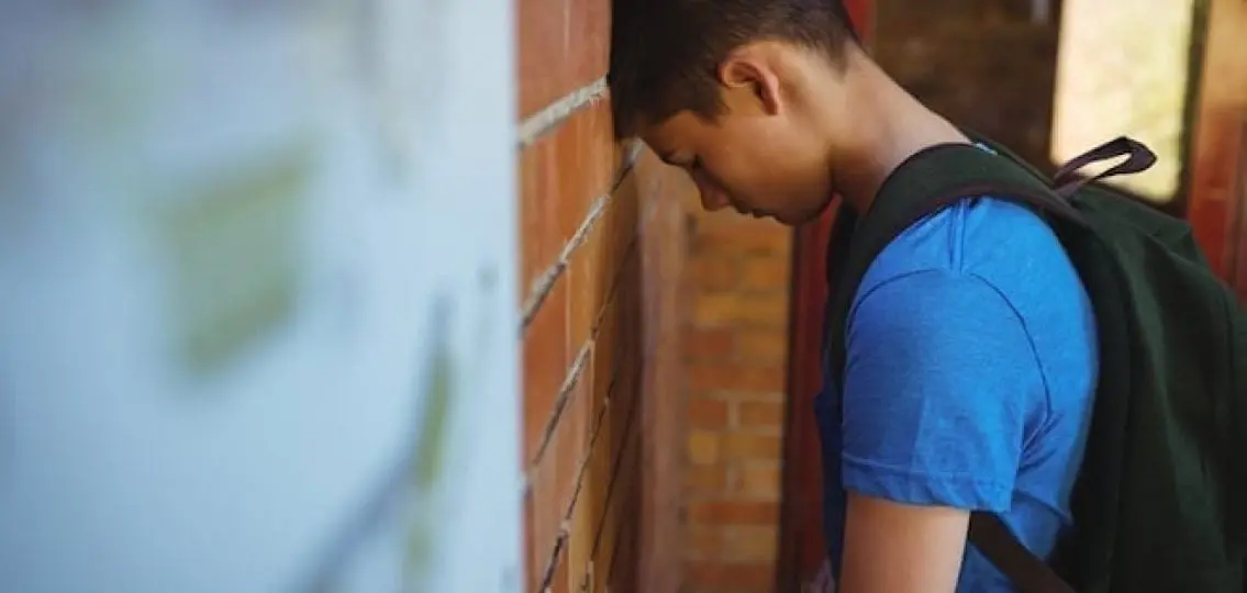 upset teen boy leaning his head against a brick wall