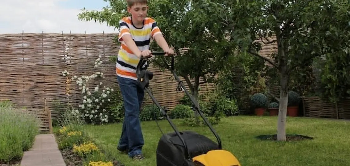 teenage boy mowing the lawn frowning on a summer day