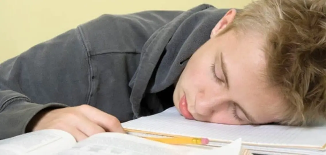 tired teenage boy asleep on top of his homework