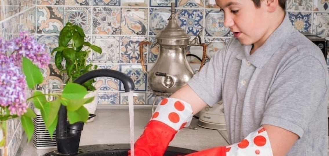 teen boy doing chores washing dishes with rubber gloves