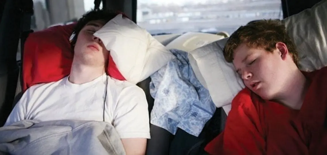 teen boys sleeping on pillows in the back of a car on a road trip