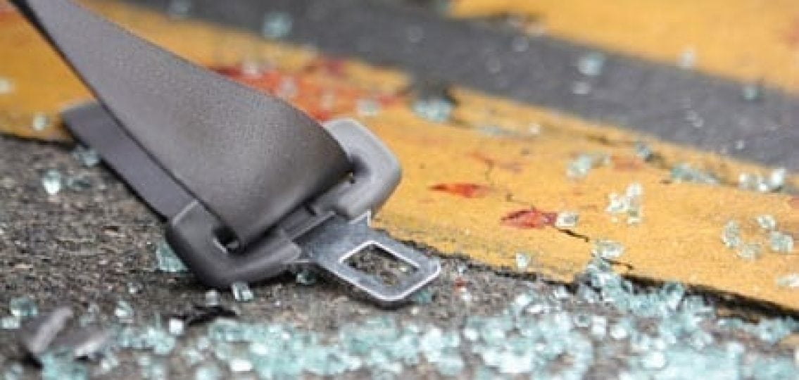 an unbuckled seatbelt next to shattered glass and blood on the street