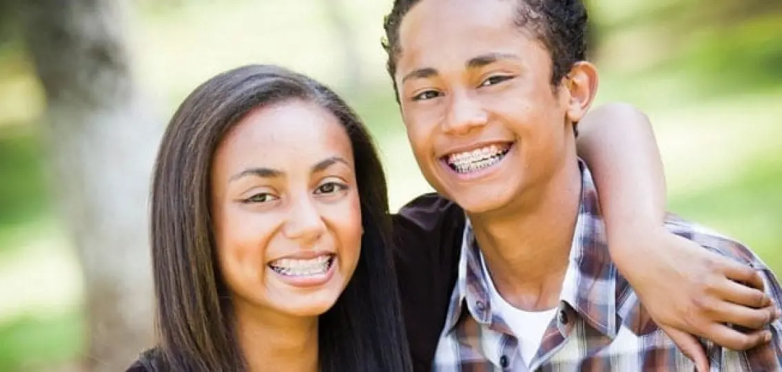 two teenagers with braces smiling outdoors
