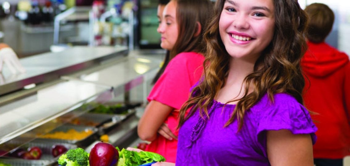 teenage girl in the cafeteria with a plate of vegetables and fruits