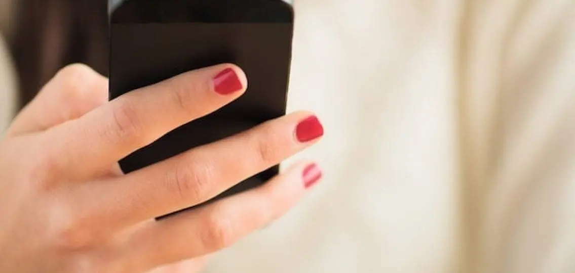close up of a hand with nail polish texting on a phone