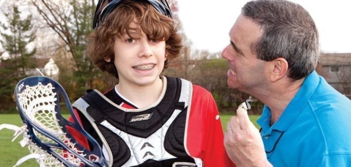 coach furiously yelling at a nervous teen lacrosse player with braces outdoors