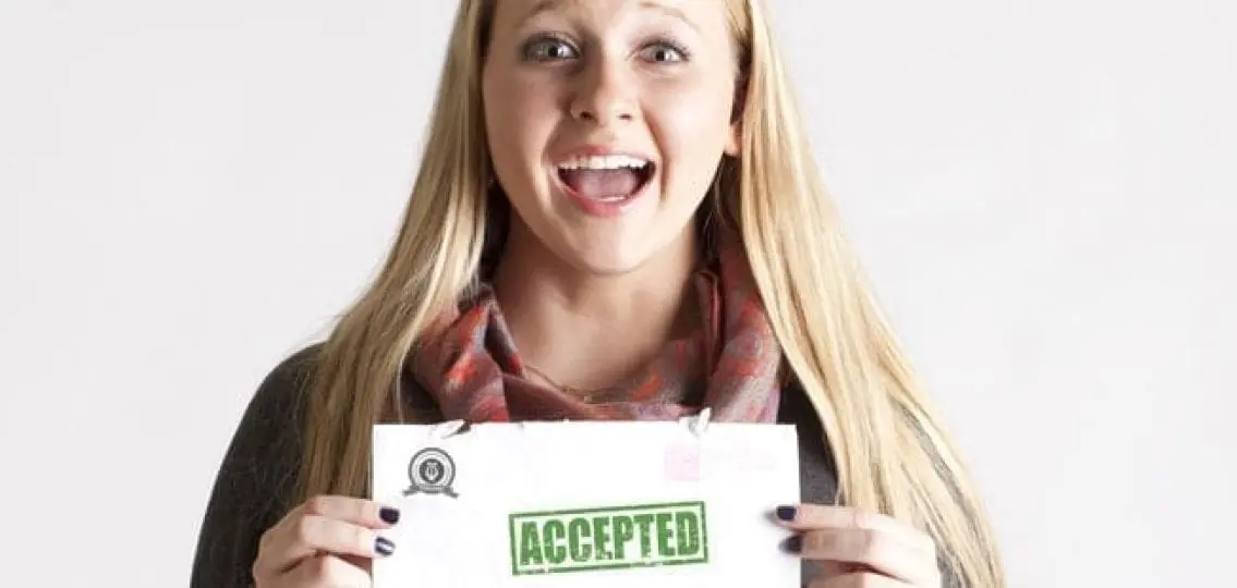 teen girl smiling excitedly and holding up a college acceptance letter