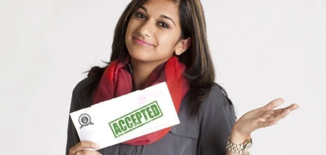 young woman shrugging with a smile holding a college acceptance letter
