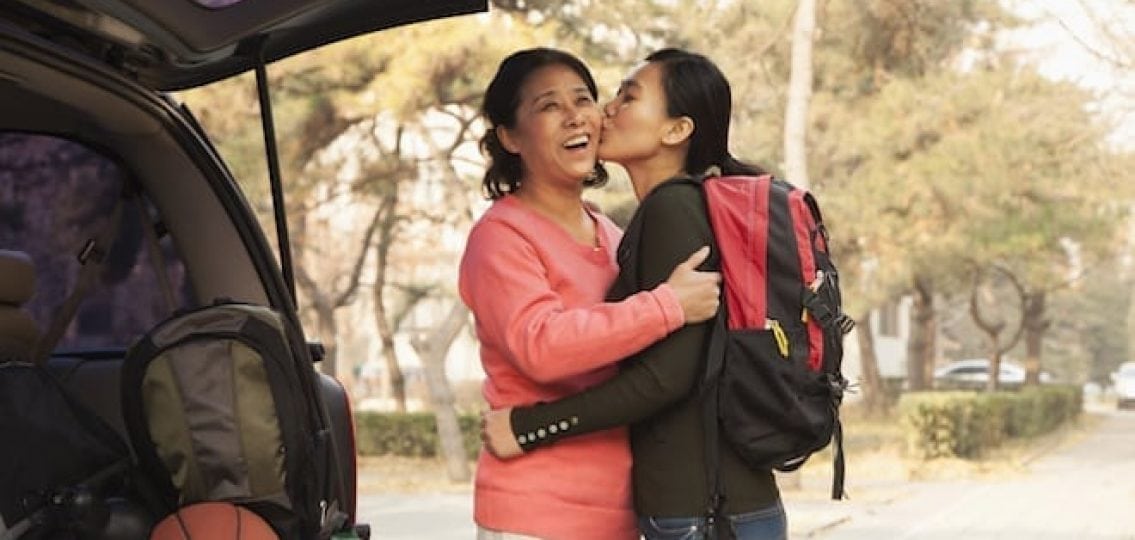 college freshman kissing her mom on the cheek in front of a packed car