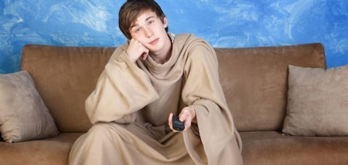 teenage boy in a snuggie lazily watching tv on the couch