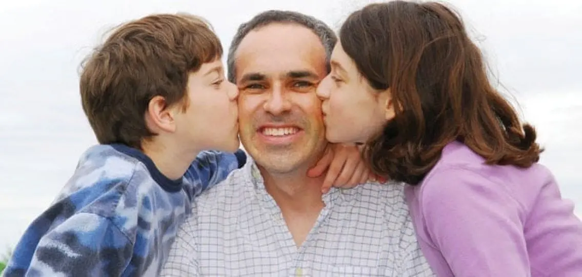 two kids kissing their dad on the cheeks