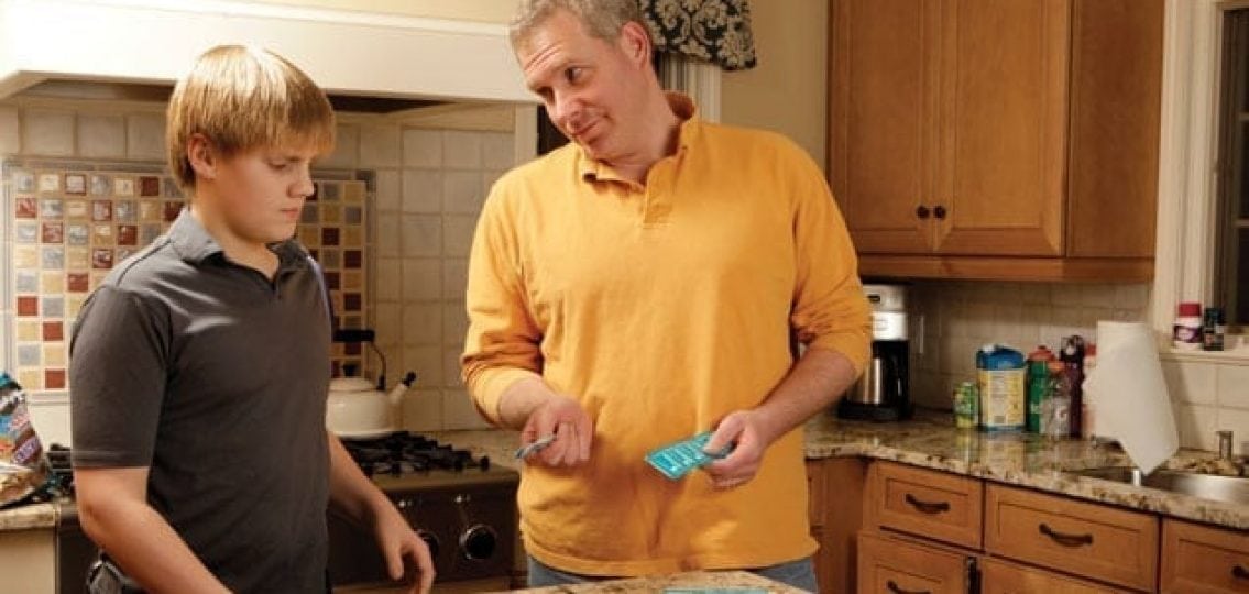 dad having The Talk showing son condoms while son looks unhappy