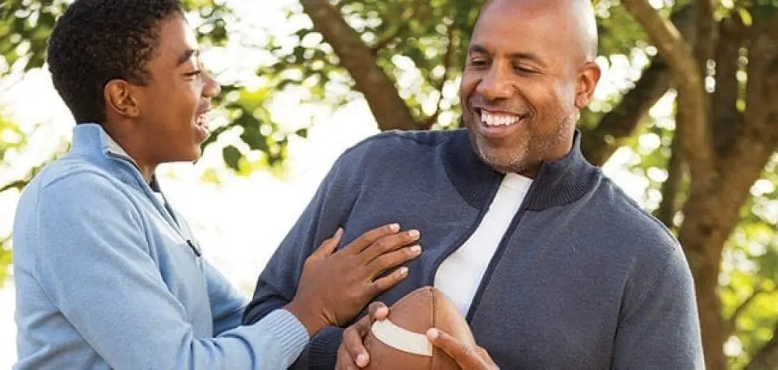 teen boy with his dad holding a football and smiling