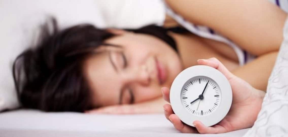sleeping teenage girl in bed holding an analogue clock