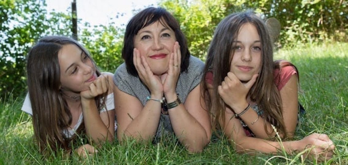 single mom posing in the grass next to her two teen daughters