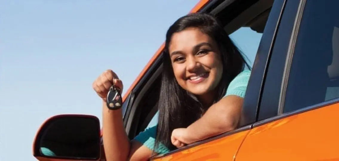 teenage girl leaning out a car window with car keys learning how to drive