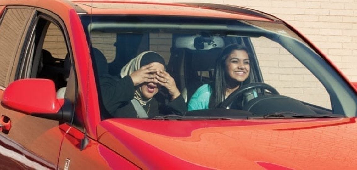 mom covering her eyes in fear while teaching her daughter to drive