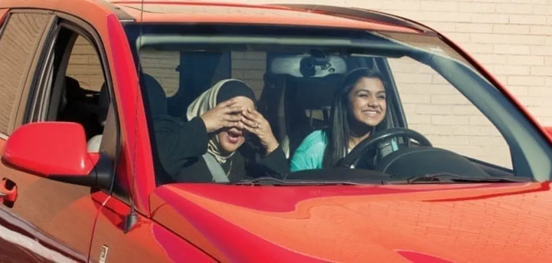 mom covering her eyes in fear while teaching her daughter to drive