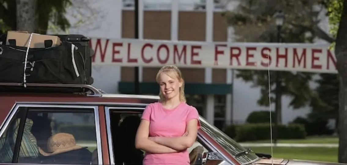 a college student in front of a packed car in front of a banner saying Welcome Freshmen