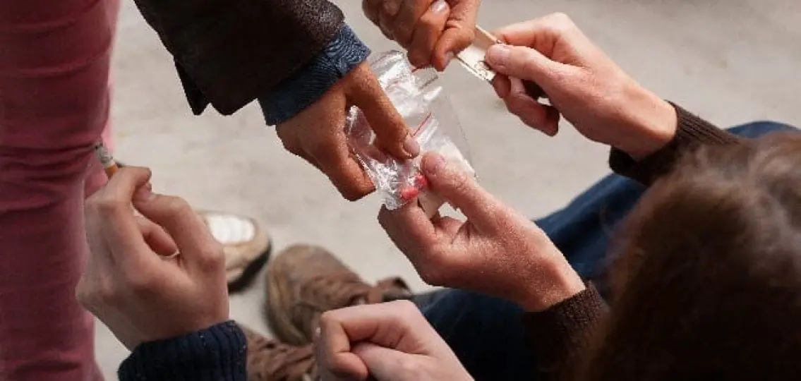 close up of someone paying cash and receiving ziplock baggies of pills while smoking a cigarette