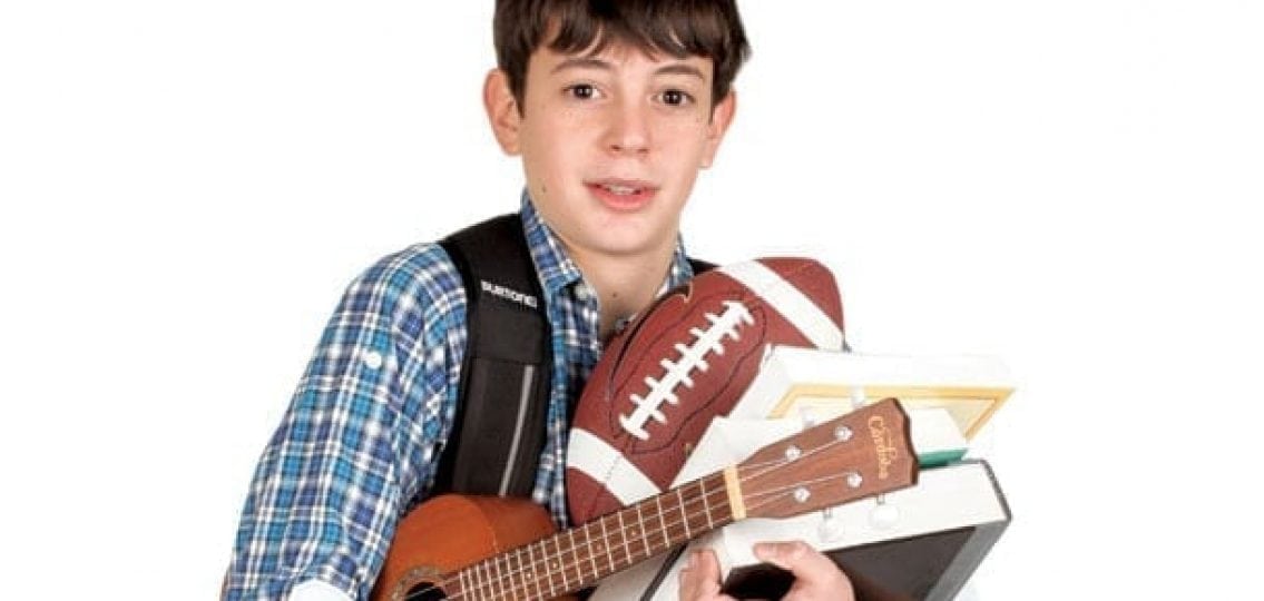 overwhelmed teen boy carrying books a football and a guitar