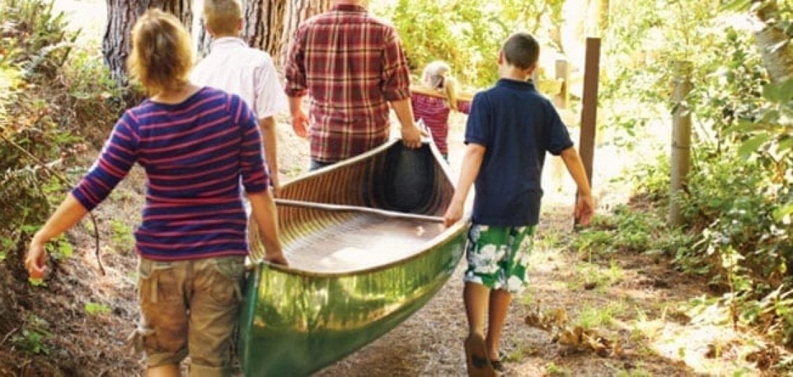 family on a camping trip carrying a canoe to a river