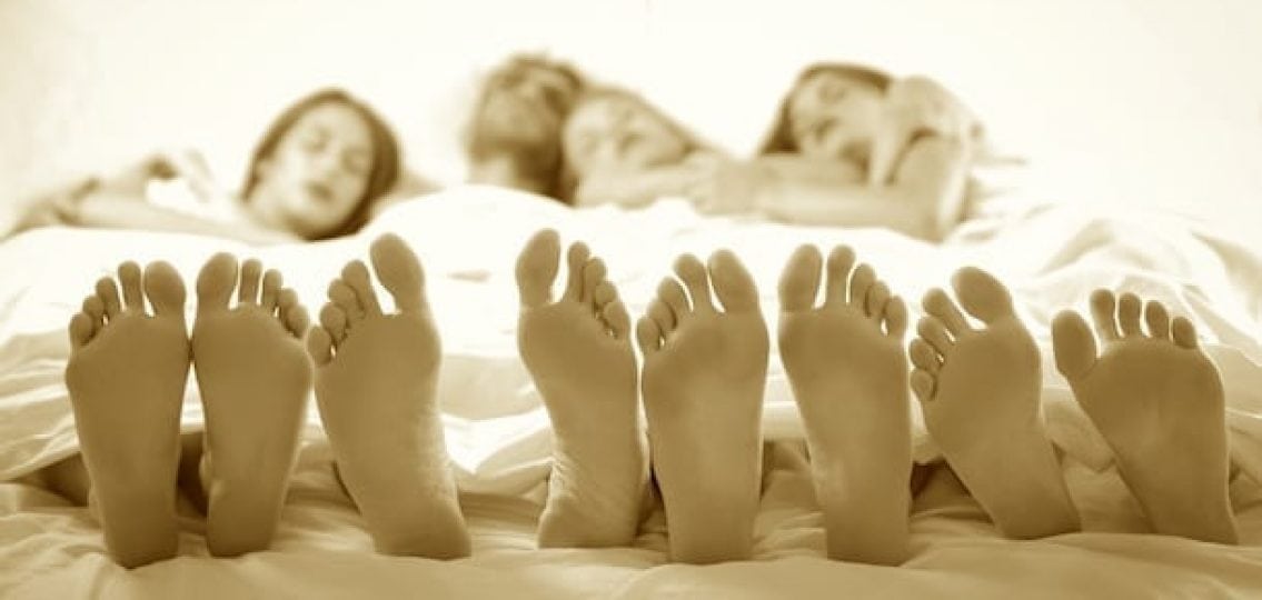 family of four sleeping together in a bed sepia tone