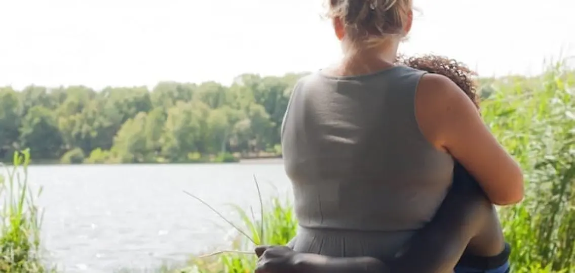 interracial family mom and daughter hugging looking at a lake